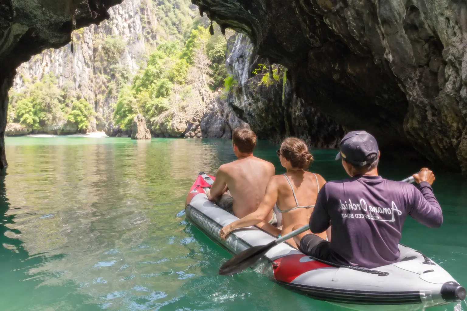 European couple canoeing through a limestone cave and lagoon at Hong Island in Phang Nga Bay with a local paddler