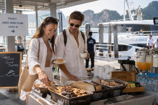 Couple enjoying a light breakfast at Chalong Pier before boarding the James Bond Island luxury power catamaran tour from Phuket