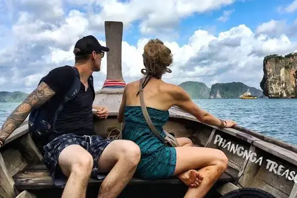 Tourists riding a traditional Thai long-tail boat through the limestone scenery of Phang Nga Bay