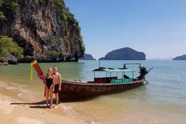 European couple standing beside a traditional Thai long-tail boat on a beach in Phang Nga Bay