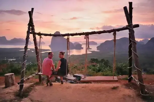 Couple sitting on a swing at Samet Nangshe Viewpoint during sunrise over Phang Nga Bay
