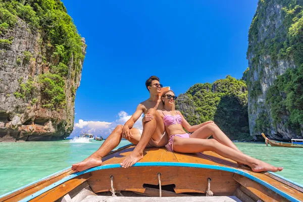 Couple relaxing on a traditional long-tail boat surrounded by limestone cliffs in the Phi Phi Islands