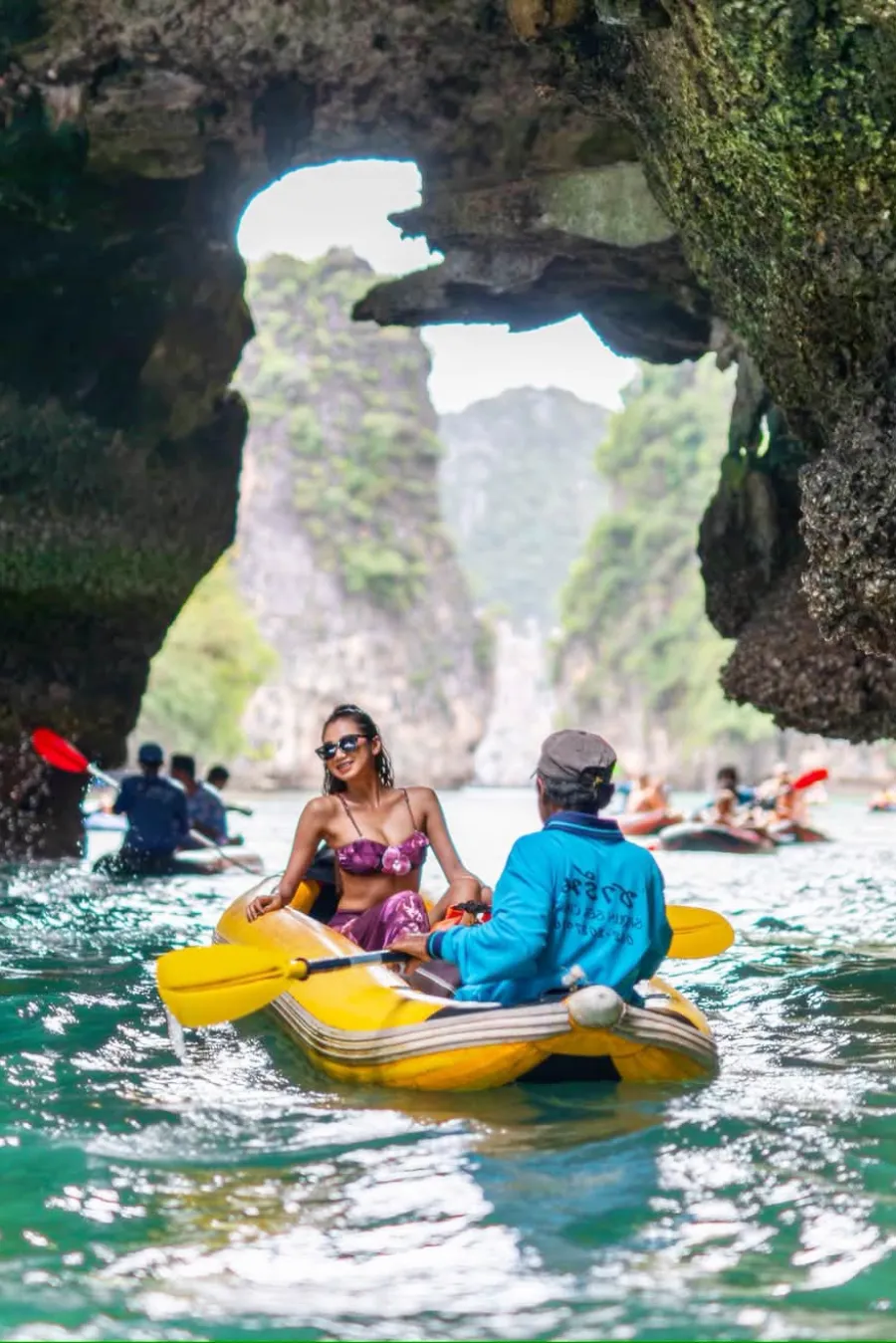 Tourist enjoying guide-paddled sea canoeing beneath a limestone cave opening in Phang Nga Bay