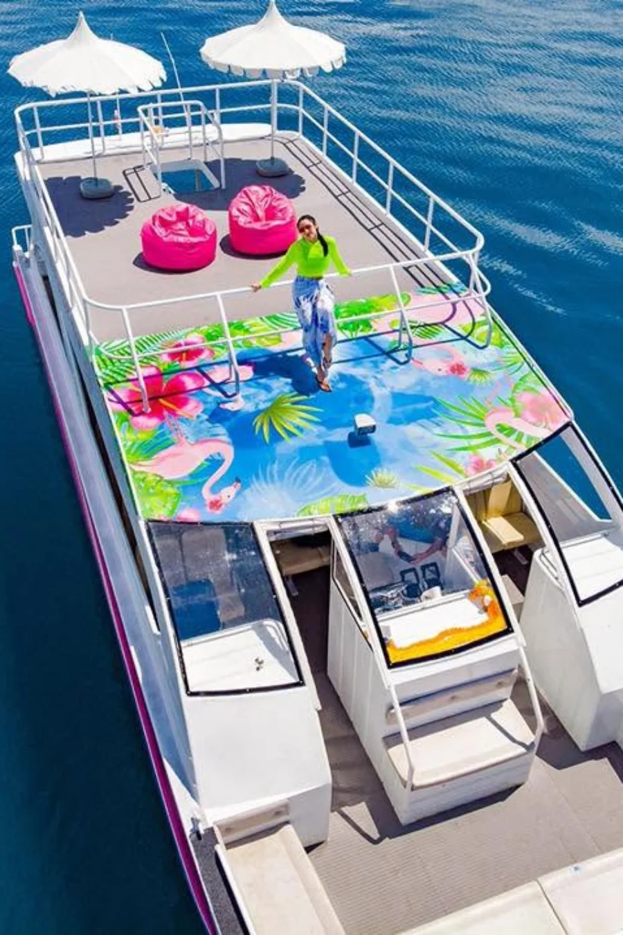 Open-air speed catamaran upper deck with sun umbrellas and pink lounge seats above the blue sea