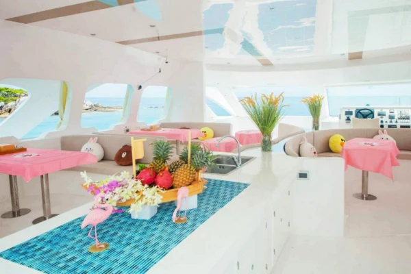 Bright luxury catamaran interior with comfortable lounge seating, dining tables and tropical fruit during a Phi Phi Island tour