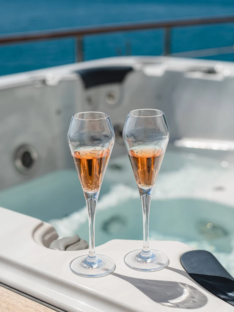 Two elegant glasses of sparkling drinks beside a relaxing jacuzzi area on a yacht overlooking the sea