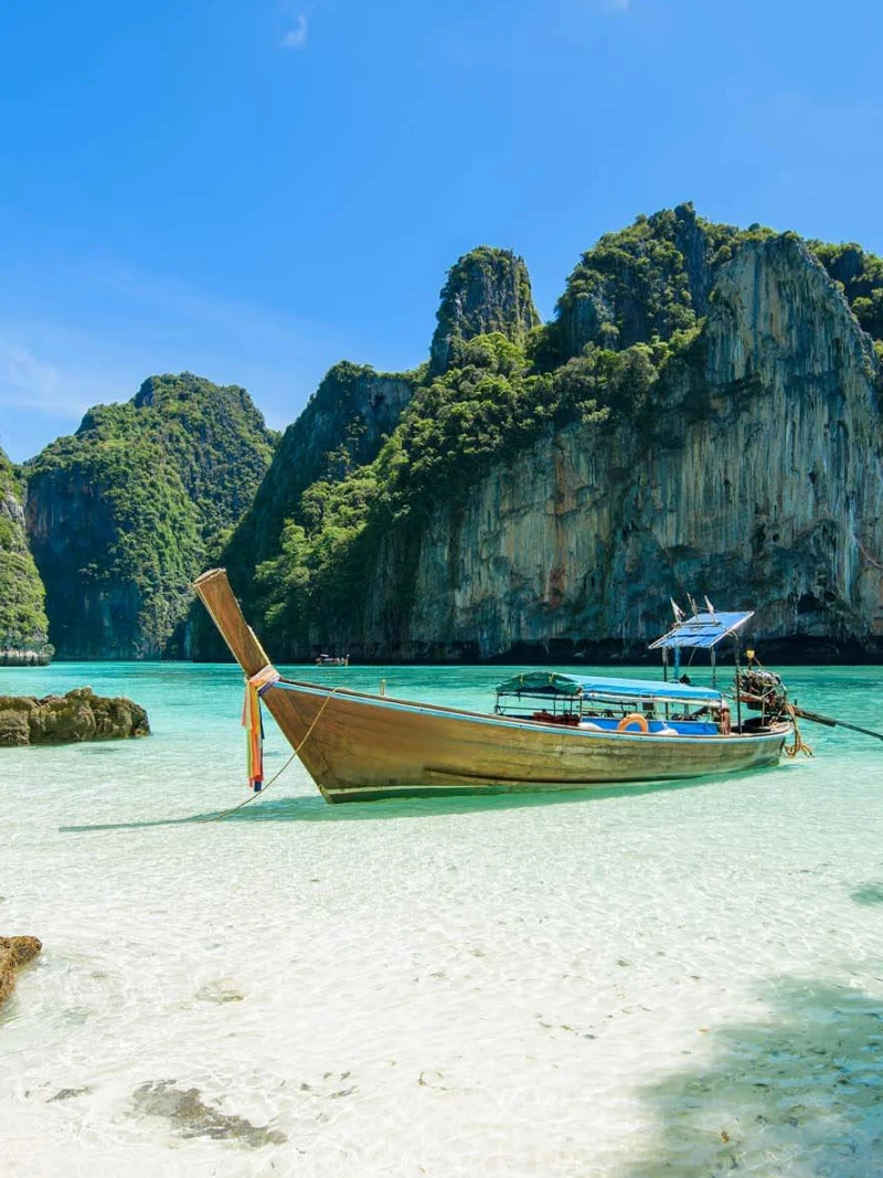 Traditional Thai longtail boat floating in clear turquoise water beneath limestone cliffs in the Phi Phi Islands